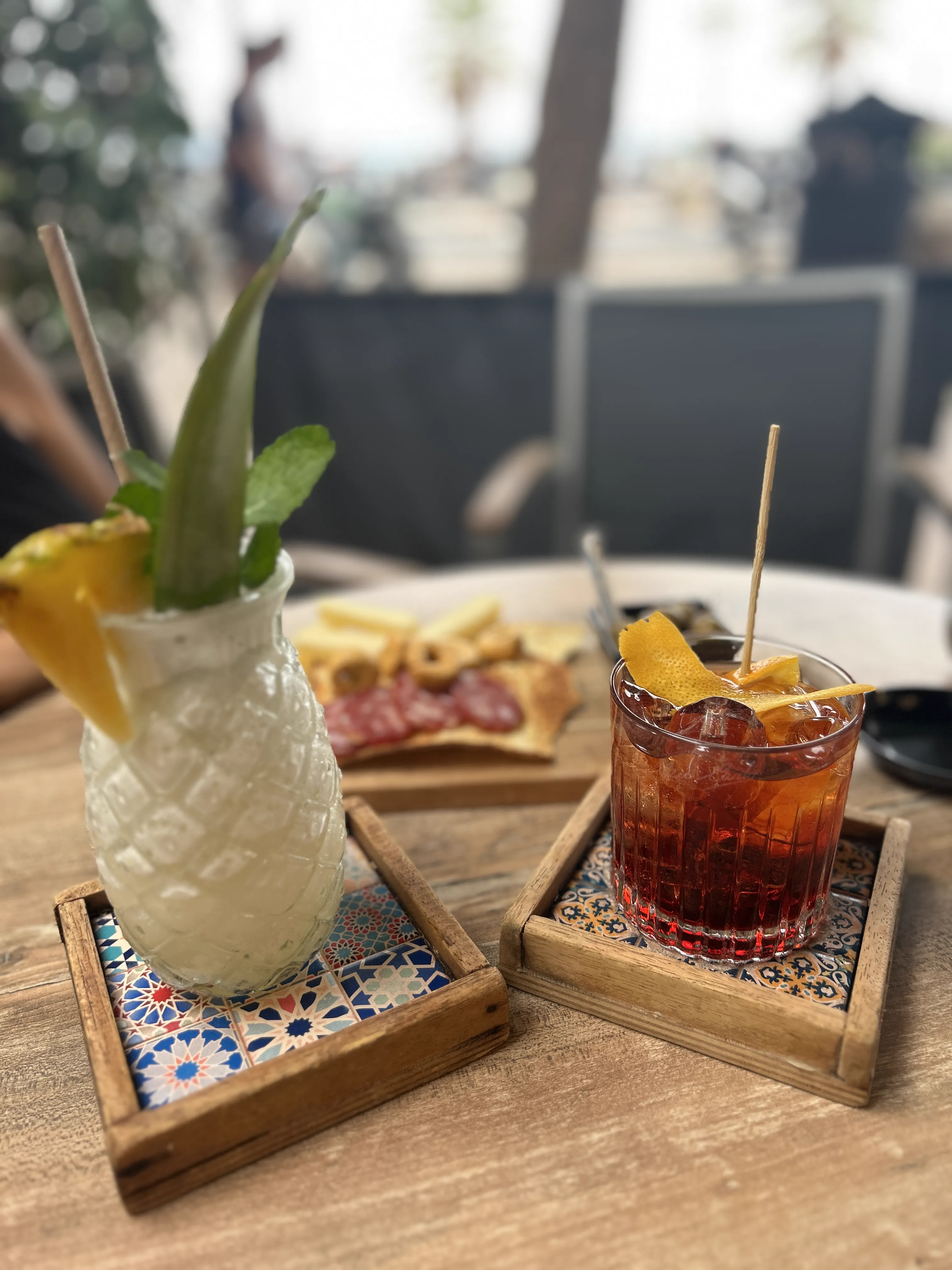 Zwei Drinks und ein Teller mit Häppchen auf einer Terrasse am Abend